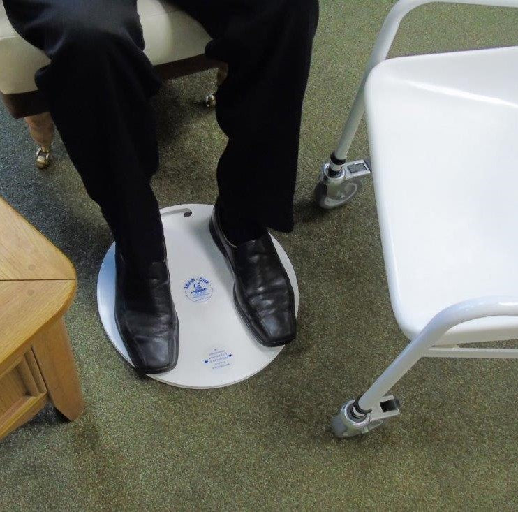 Person wearing black shoes stepping on a round white medidisk platform with a logo on a green carpeted floor.