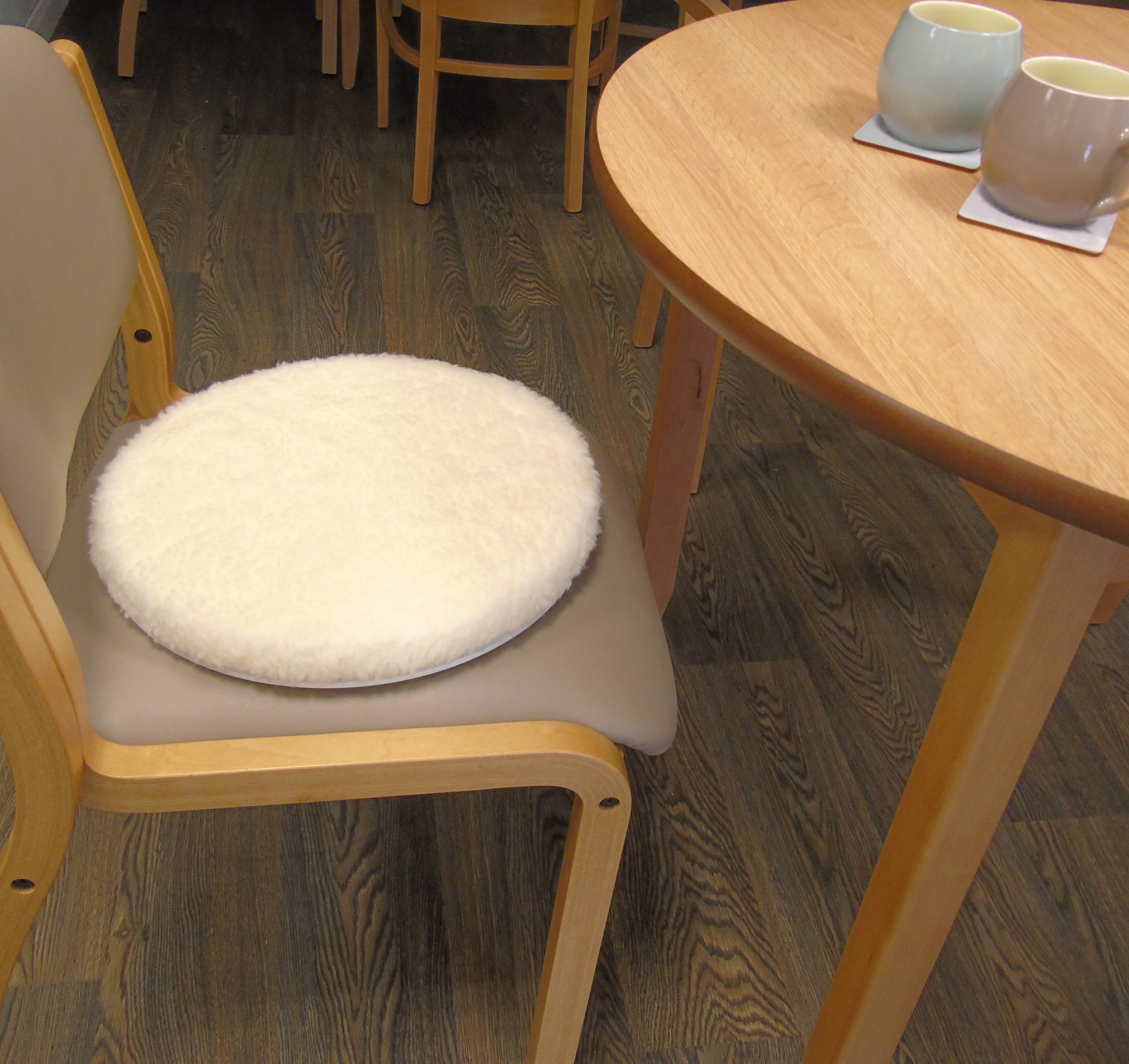 Chair with a white turning disk cushion on a wooden floor next to a table with two cups.