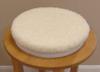 Round wooden stool with a white turning cushion on a plain background