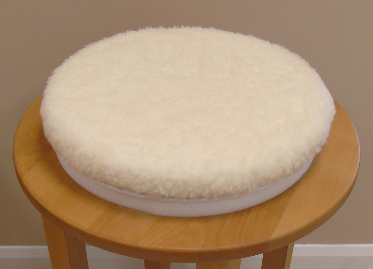 Round wooden stool with a white turning cushion on a plain background